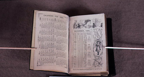 Pages of a volume held open by sticks.