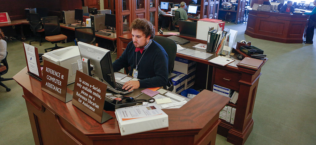 A man sitting at the reference desk while on a computer