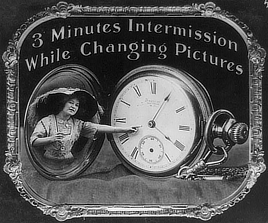 Black and white photo shows a woman pointing at a large pocket watch dial.
