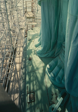 The feet of the Statue of Liberty are surrounded by scaffolding in a colorful view from above.
