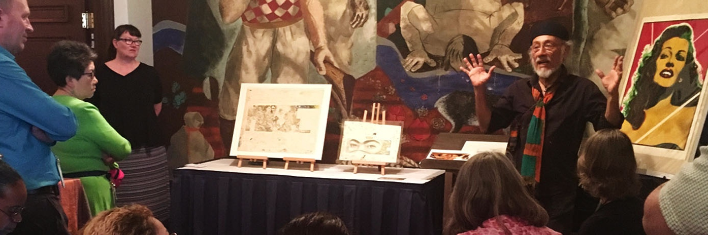 Color photograph of artist instructing crowd with posters and frescos in background
